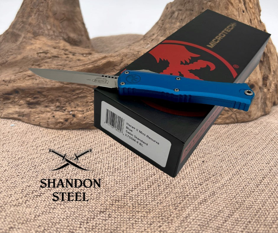 A Microtech Mini Hera II knife with a blue handle and satin finished blade, displayed on top of its packaging box with the brand name Primemartshop visible.