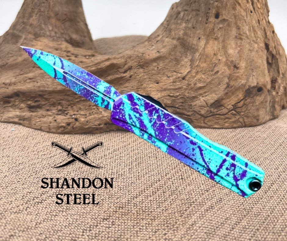 Blue and purple patterned knife on a wooden background with Primemartshop branding.